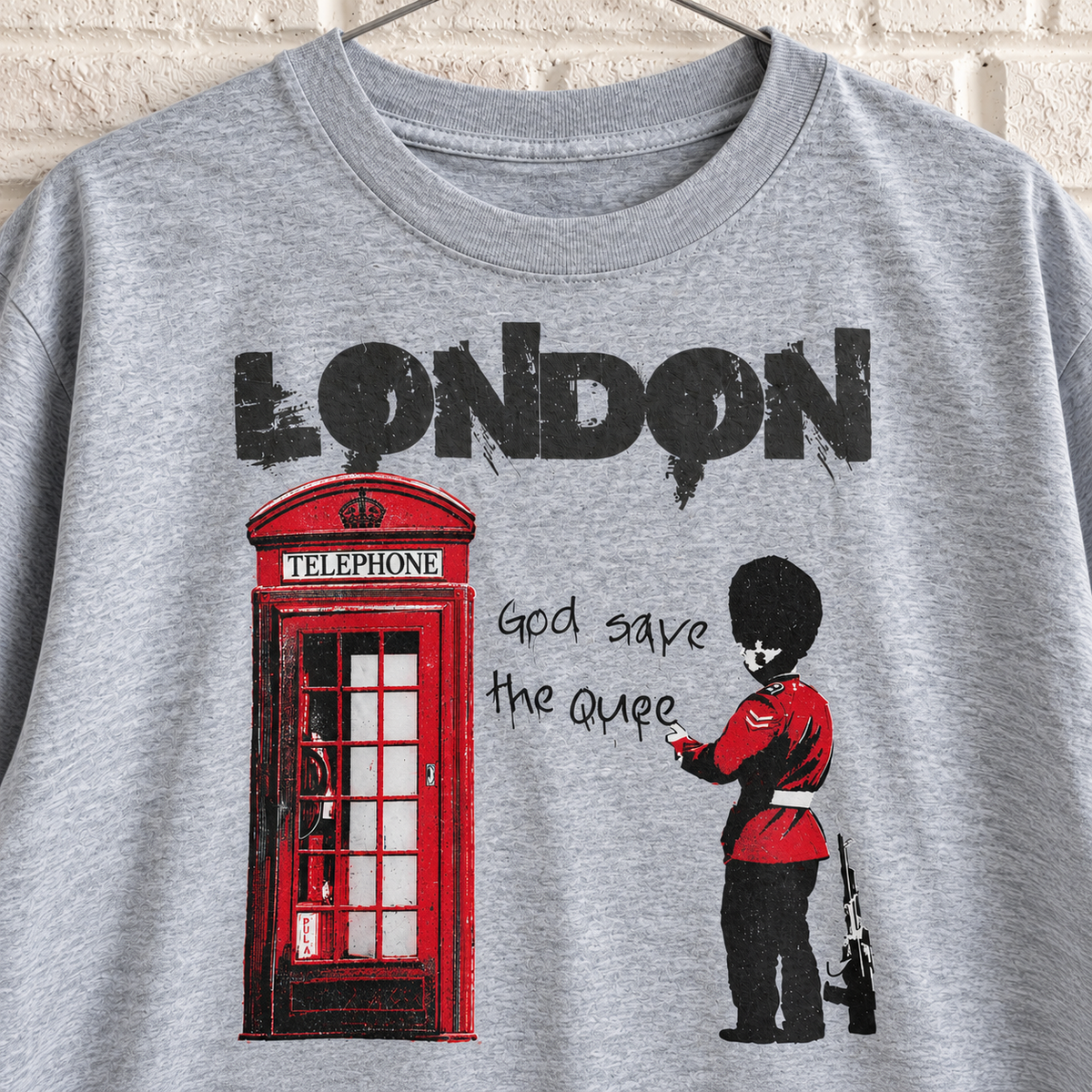 Grey London phone box and guard graphic tee on a white brick wall with a wire hanger — close-up front view