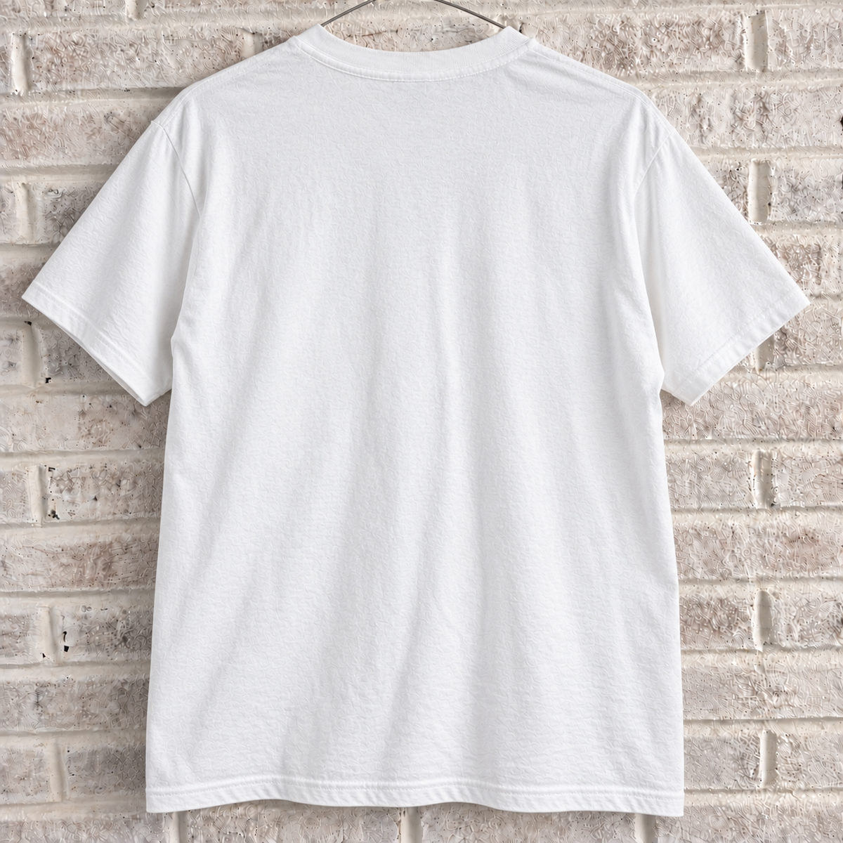 White New York skyline and theatre masks graphic tee on a white brick wall with a wire hanger — blank back view