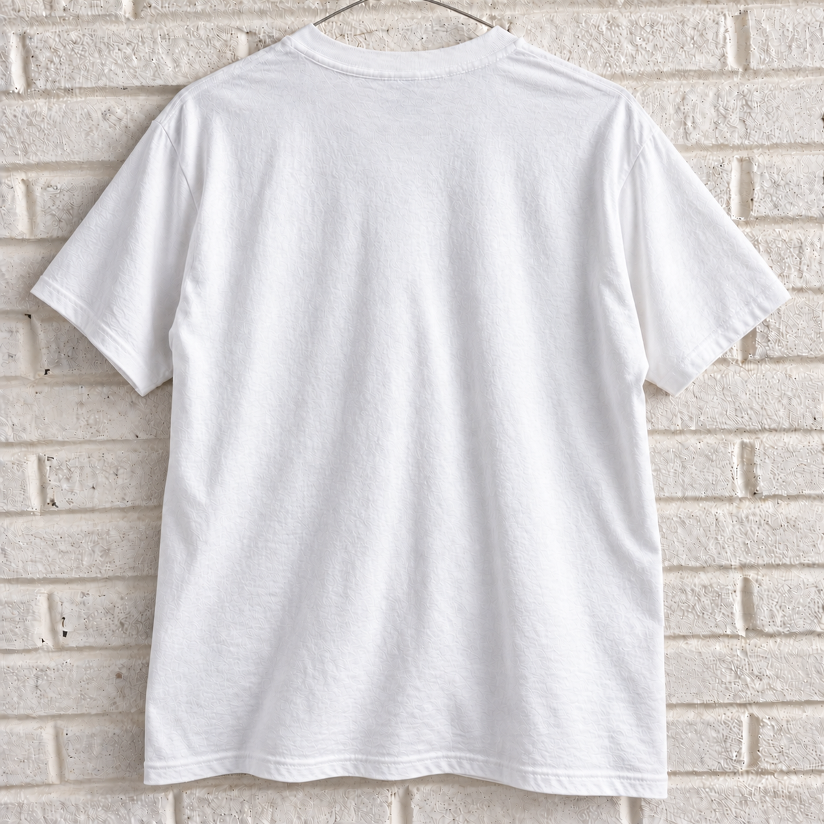 White New York skyline and theatre masks graphic tee on a white brick wall with a wire hanger — blank back view
