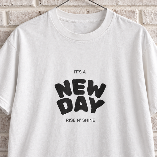 White Comfort Colors graphic tee on a white brick wall with a wire hanger — close-up front view