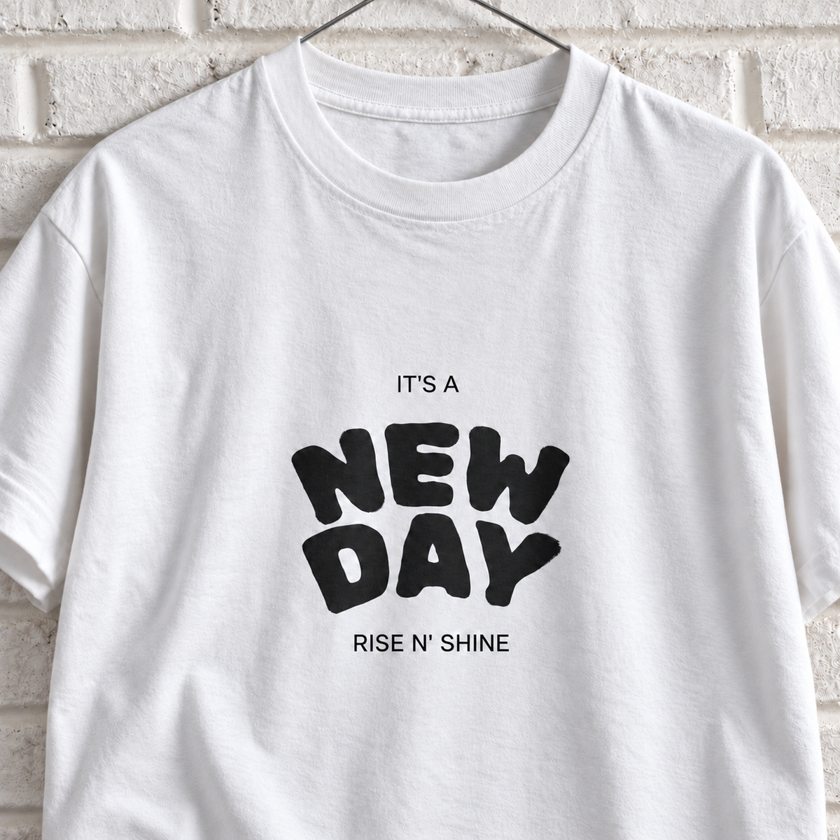 White Comfort Colors graphic tee on a white brick wall with a wire hanger — close-up front view