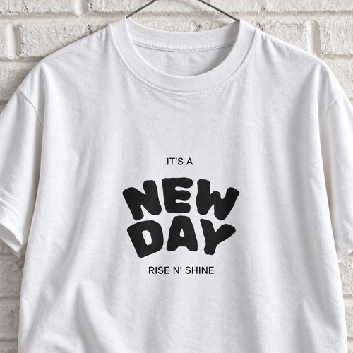 White Comfort Colors graphic tee on a white brick wall with a wire hanger — close-up front view