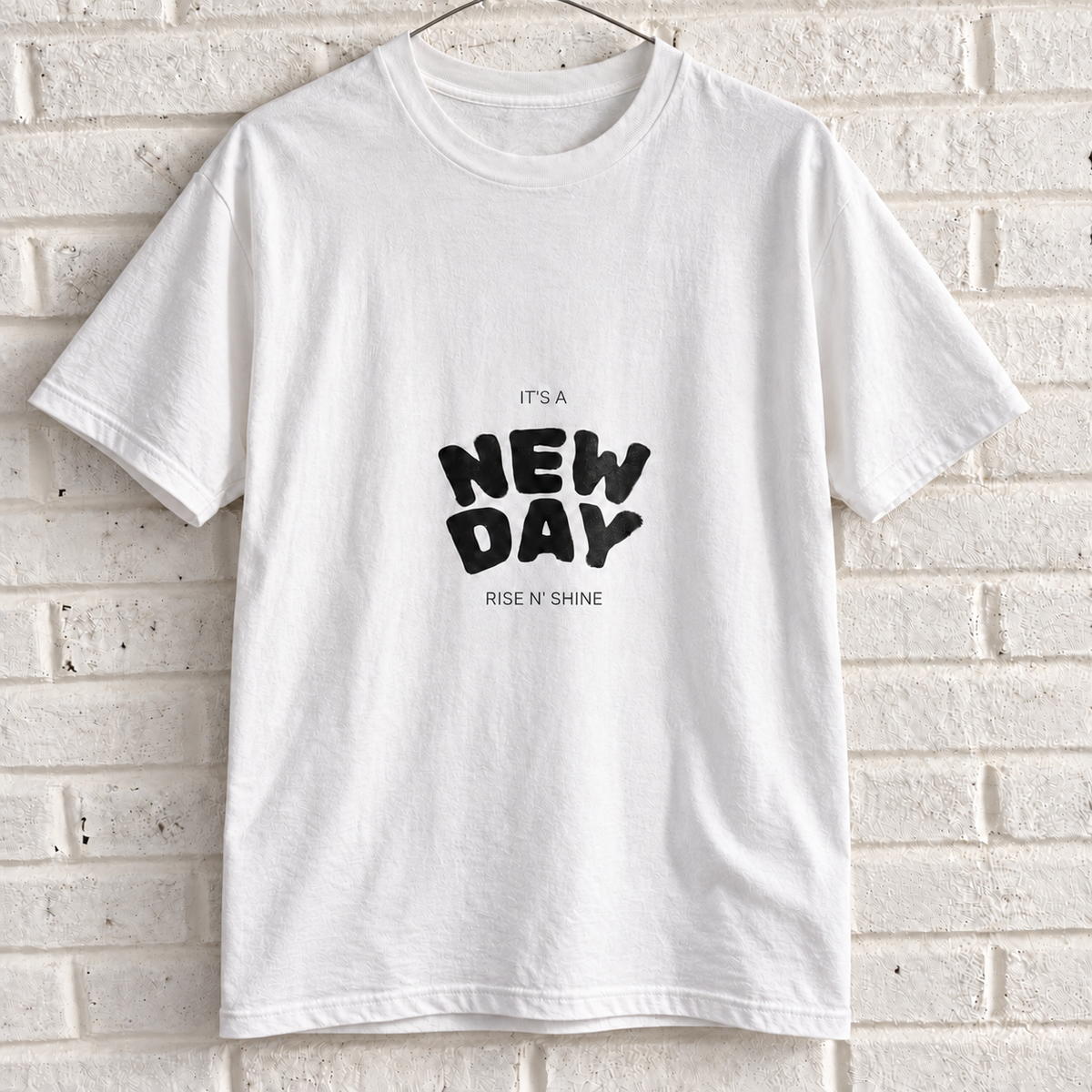 White Comfort Colors graphic tee on a white brick wall with a wire hanger — front view